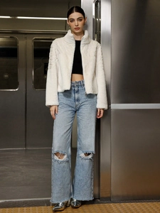Faux fur high collar jacket paired with ripped jeans and metallic boots in industrial setting