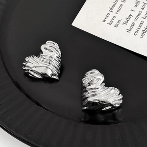 Detailed view of silver heart-shaped stud earrings with textured metallic stripe surface