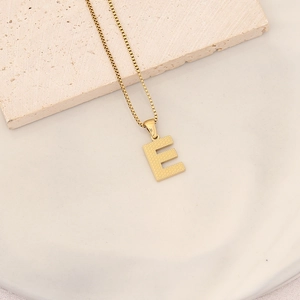 Macro shot of textured gold letter E pendant on a matching box chain over stone