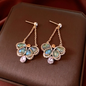 Close-up of vintage earrings with green crystals and a pink teardrop glass pendant