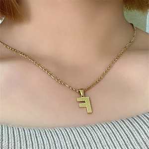 Dettaglio di una collana a catena Figaro dorata con ciondolo a lettera F su una modella