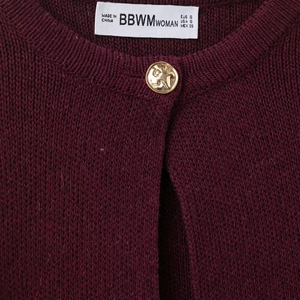Women's knit cardigan in dark red with golden crest buttons and fringe accents