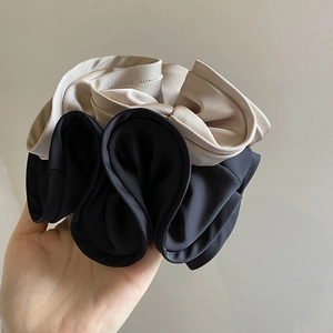 Close-up of oversized black and beige satin scrunchies with ruffled texture and soft fabric