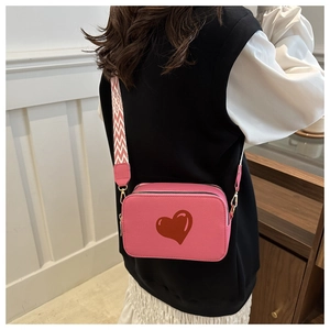 Detail of pink crossbody bag featuring a red heart pattern and wide textured strap