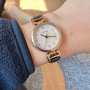 Detail of elegant gold watch with rhinestone accents and black slim leather strap on wrist
