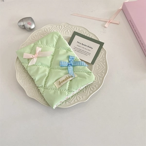 Close-up of mint green quilted passport holder with pink bow on an embossed plate
