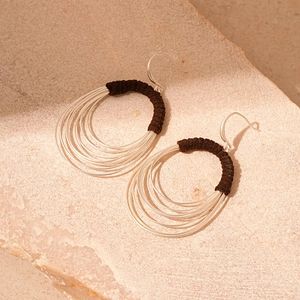 Macro detail of layered silver hoop earrings with dark brown fabric winding and texture