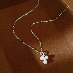 Elegant silver chain necklace with three white pearls and a sparkling zircon on a brown tray