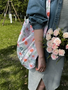 Outdoor shot of floral cotton tote bag featuring large pink flowers on a green lawn