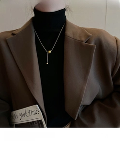 Detailed view of a gold spherical bead pendant necklace on a model wearing a brown blazer