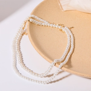 Elegant double-layered white faux pearl necklace with gold metal clasp on a ceramic dish