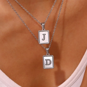 Close-up of double layered silver necklaces with white shell rectangular J and D pendants