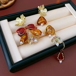 Detail of amber teardrop earrings with red ribbon bow and white pearls on beige cushion