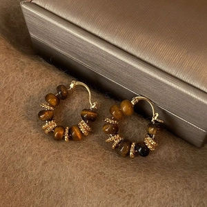 Golden hoop earrings with tiger eye beads on a warm brown velvet background