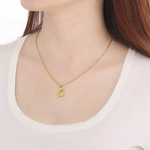 Close-up of golden 18K heart pendant with bird engraving worn on a necklace