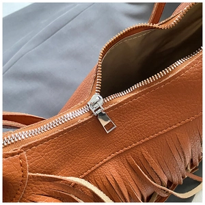 Close-up of brown leather bag featuring fine stitching and silver metal zipper details