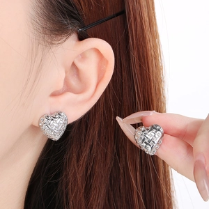 Detailed close-up of silver heart stud earrings featuring woven texture and small gems