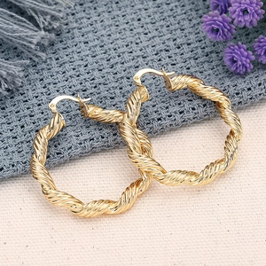 Dettaglio di orecchini a cerchio dorati con texture a spirale e finitura in metallo punk