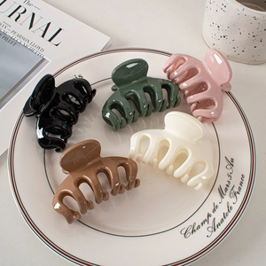 Overhead view of five glossy plastic hair claws in black, green, pink, brown, and cream