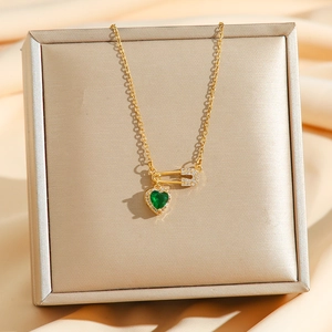 Elegant gold safety pin necklace with green heart pendant on luxury champagne silk