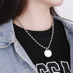 Gros plan d'un collier à billes argenté avec pendentif disque rond sur un mannequin