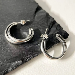 Detailed view of silver double-layered C-shaped hoop earrings on a black stone plate