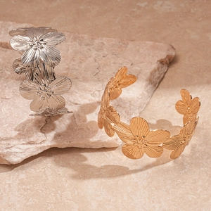 Detail of gold and silver floral cuff bracelets with brushed texture on natural stone