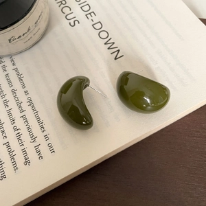 Detailed close-up of dark green resin bean earrings resting on an open book surface