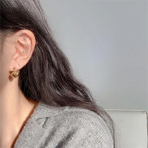 Close-up of a elegant golden heart drop earring worn by a model in a gray sweater