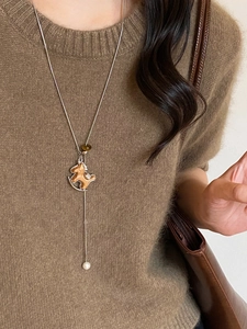 Close-up of wooden horse pendant and pearl on silver necklace worn over a sweater