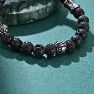 Lava stone bead bracelet with silver steel totem charms on a natural rock backdrop