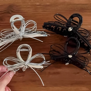 Silver and black metal bow hair claws shown on a wooden table for women hair styling