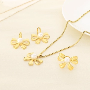 Elegant gold bow jewelry set with pearls featuring necklace earrings and ring on fabric