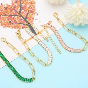 Detail view of gold paperclip chain bracelets with rectangular zircon in emerald and pink