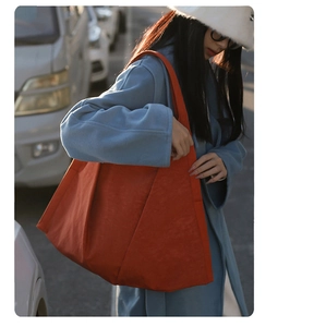 Close-up of a large orange suede tote bag worn by a model in a stylish street setting