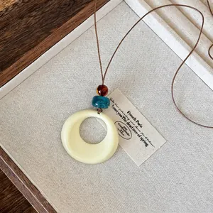 Close-up of cream resin circular pendant with amber and teal beads on brown wax cord
