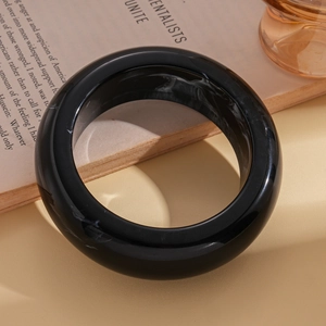 Minimalist wide black resin bangle with white marble pattern on a chic beige background