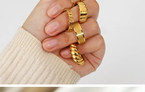 Close-up of a hand wearing multiple gold-plated stainless steel rings with unique textures