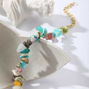 Detail of colorful natural gemstone fragments with gold metal clasp on textured base