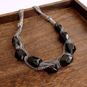Macro view of multi-layered silver chains with large black faceted acrylic gemstones
