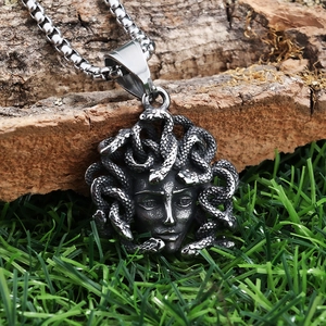 Macro shot of silver Medusa relief pendant on natural bark with green grass detail