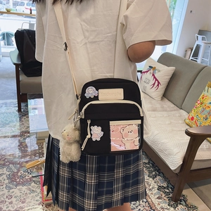 Détail du sac à bandoulière en toile noire avec écussons mignons et pendentif en peluche