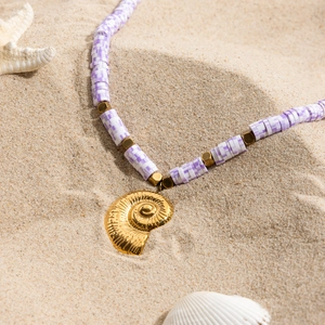 Détail du collier en argile polymère violette avec pendentif coquillage doré sur sable