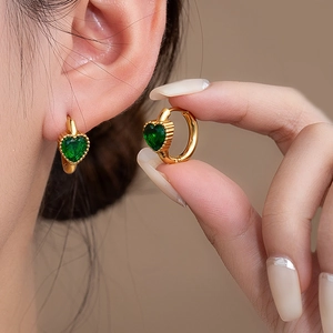Macro shot of heart-shaped emerald stone earrings with gold huggie hoop and pavé setting