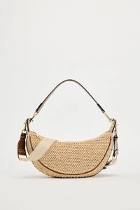 Detail of woven half-moon bag with brown leather trim and beige canvas crossbody strap