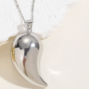 Macro shot of polished silver teardrop pendant resting on a textured white stone surface