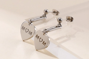 Close-up of silver steel heart earrings with MOM engraving and ball stud detail