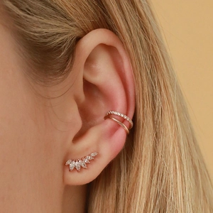 Close-up of rose gold wing-shaped stud earrings and sparkling zircon ear cuff on ear