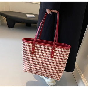 Close-up of red houndstooth tote bag with sturdy handles and golden rivet details