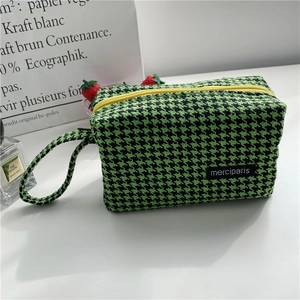 Detail of green houndstooth tweed pouch with yellow zipper and merci logo label